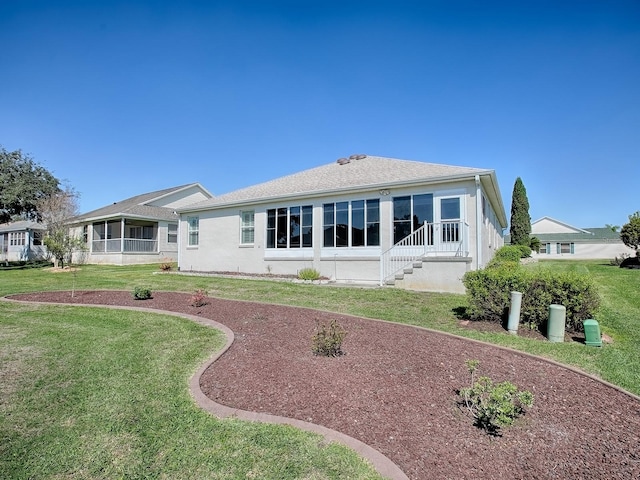 back of house featuring a sunroom, a lawn, and stucco siding