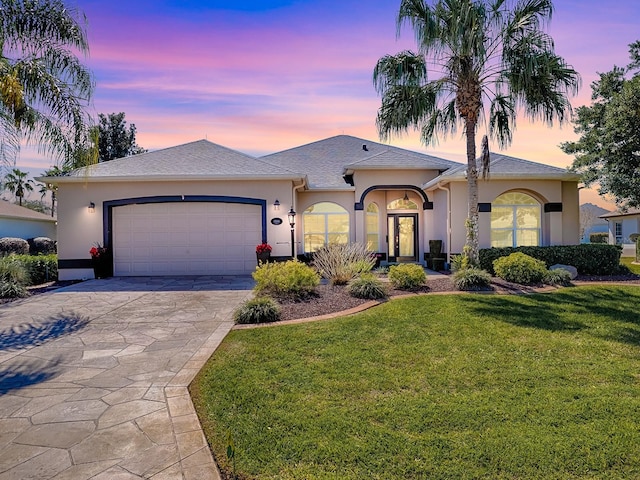 ranch-style home with driveway, an attached garage, a lawn, and stucco siding