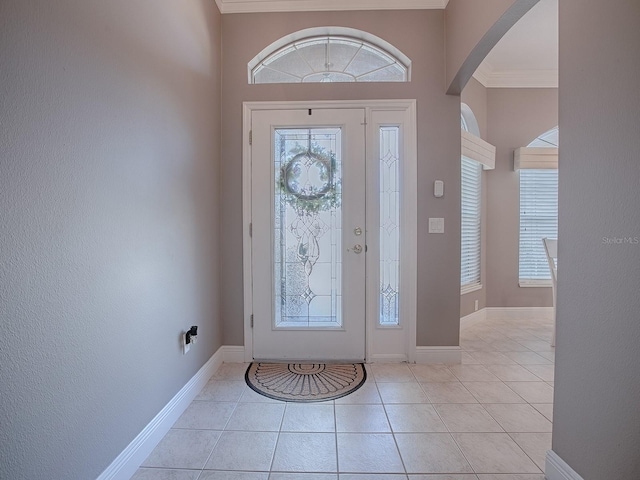 entrance foyer featuring light tile patterned floors, baseboards, arched walkways, and crown molding