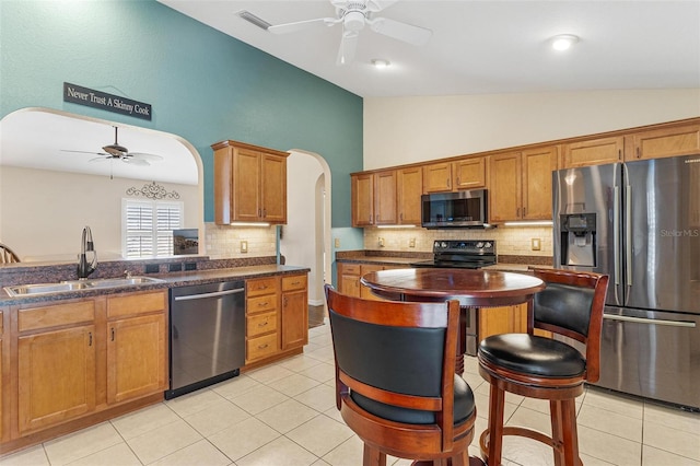 kitchen with arched walkways, lofted ceiling, a sink, appliances with stainless steel finishes, and brown cabinets