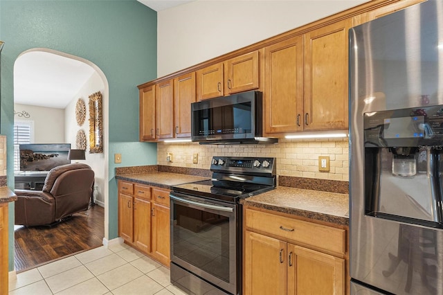 kitchen featuring brown cabinets, light tile patterned floors, stainless steel appliances, dark countertops, and tasteful backsplash