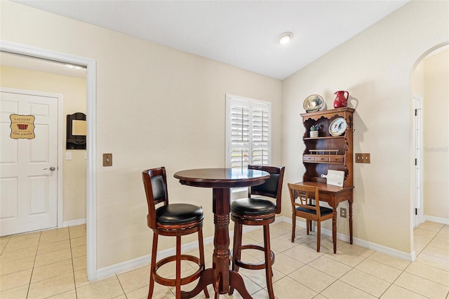 dining space with arched walkways, lofted ceiling, baseboards, and light tile patterned floors