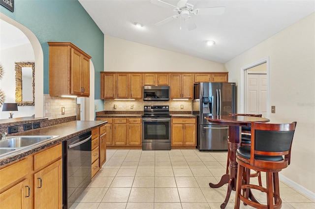 kitchen featuring lofted ceiling, backsplash, arched walkways, dark countertops, and appliances with stainless steel finishes