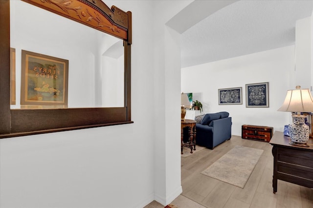 hall with a textured ceiling, arched walkways, and wood finished floors