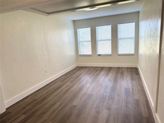 spare room featuring a textured wall, dark wood-type flooring, and baseboards