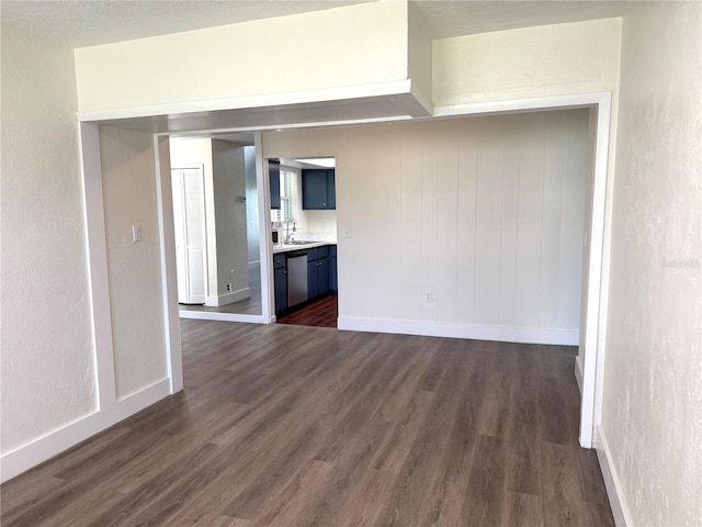 empty room with a sink, a textured wall, dark wood finished floors, and baseboards