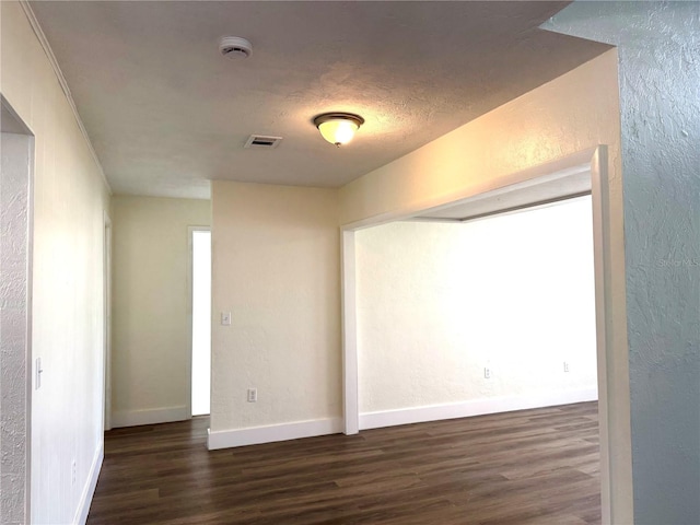 unfurnished room with baseboards, visible vents, wood finished floors, and a textured wall