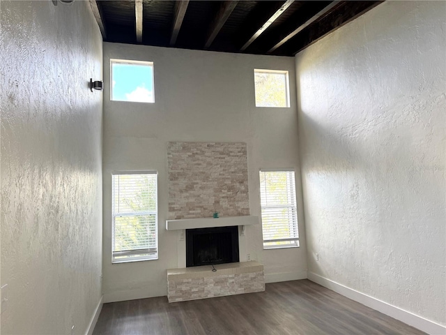 unfurnished living room with a fireplace with raised hearth, a high ceiling, wood finished floors, and a healthy amount of sunlight