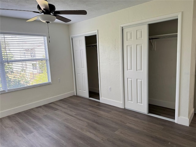 unfurnished bedroom featuring dark wood finished floors, two closets, a textured wall, ceiling fan, and baseboards