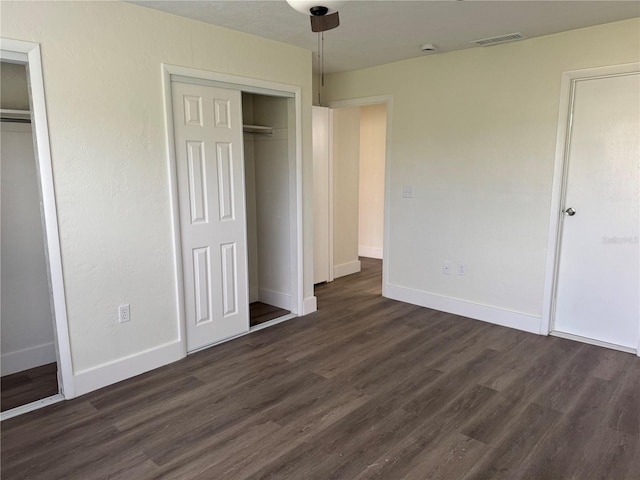 unfurnished bedroom with dark wood-style floors, visible vents, baseboards, and two closets