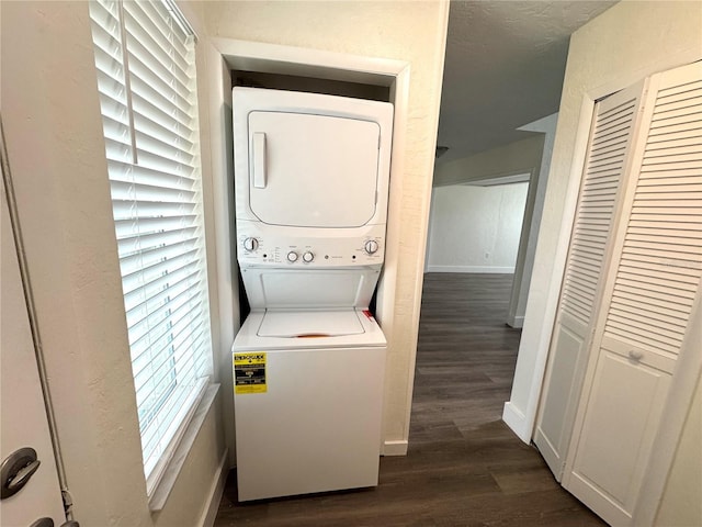 laundry area with a textured ceiling, stacked washer / dryer, dark wood finished floors, and baseboards