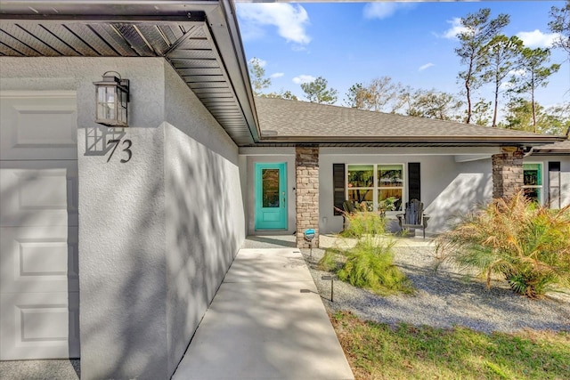 entrance to property featuring a garage, roof with shingles, and stucco siding