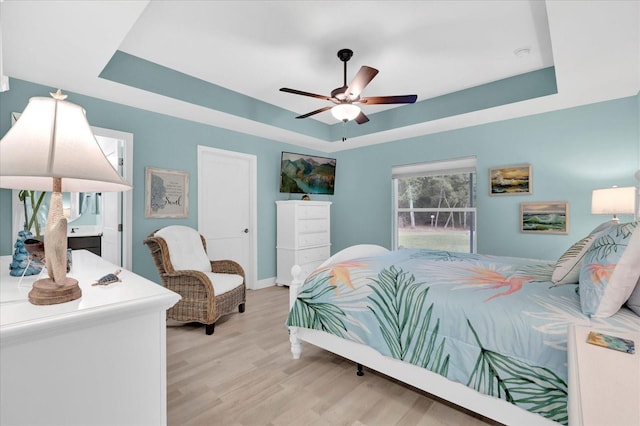 bedroom featuring light wood-type flooring, ceiling fan, and a tray ceiling