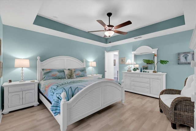 bedroom featuring light wood-type flooring, a raised ceiling, visible vents, and a ceiling fan