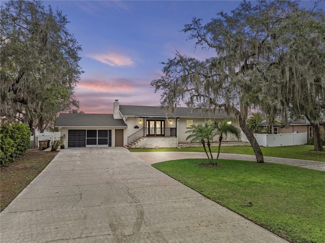 view of front of house with a yard, a chimney, concrete driveway, an attached garage, and fence