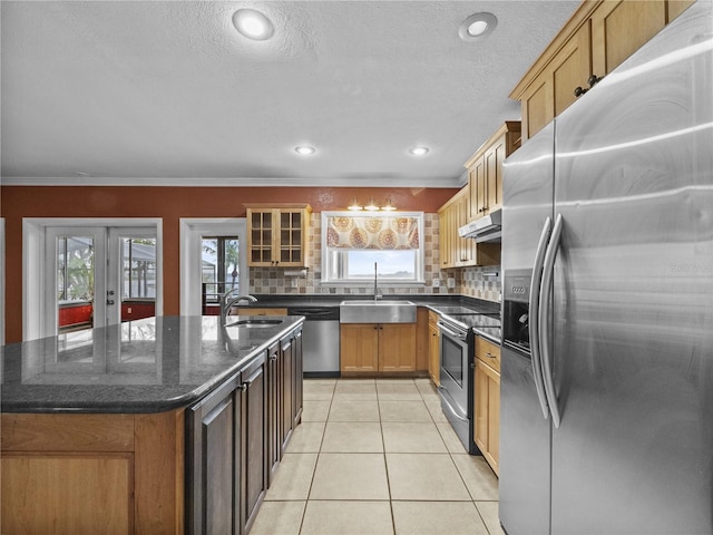 kitchen featuring light tile patterned floors, a kitchen island with sink, stainless steel appliances, under cabinet range hood, and a sink