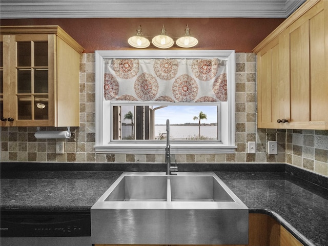 kitchen with dark countertops, a sink, backsplash, and light brown cabinetry