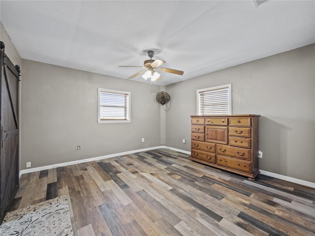 unfurnished bedroom featuring a barn door, wood finished floors, a ceiling fan, and baseboards