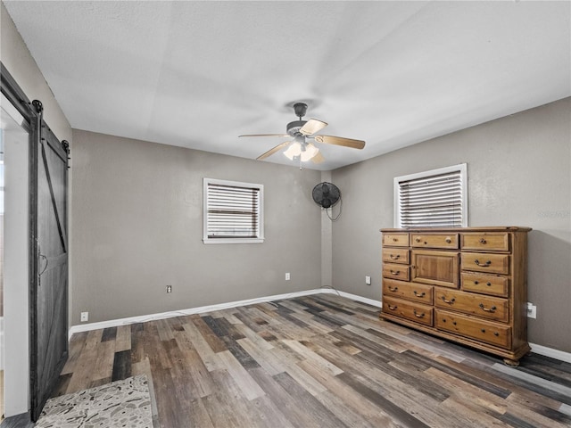 unfurnished bedroom featuring a barn door, wood finished floors, a ceiling fan, and baseboards