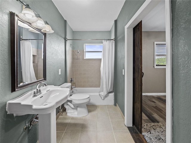 bathroom featuring shower / tub combo with curtain, a textured wall, toilet, baseboards, and tile patterned floors