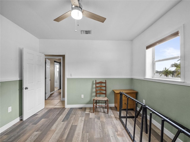 interior space featuring a ceiling fan, visible vents, baseboards, and wood finished floors