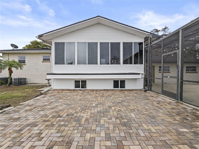 rear view of house featuring glass enclosure, a patio area, and central AC