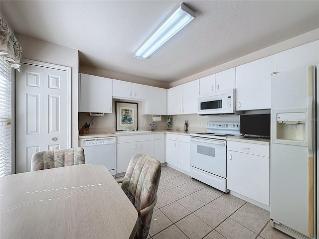 kitchen with white appliances, white cabinets, light countertops, a sink, and light tile patterned flooring