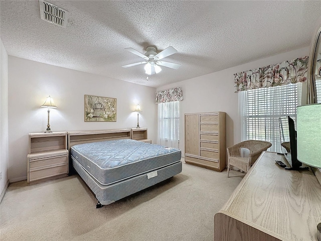 bedroom featuring visible vents, ceiling fan, light carpet, and a textured ceiling