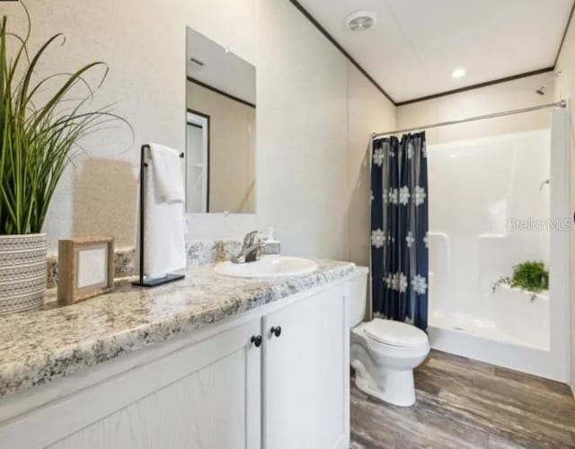 full bathroom featuring crown molding, toilet, a shower stall, vanity, and wood finished floors