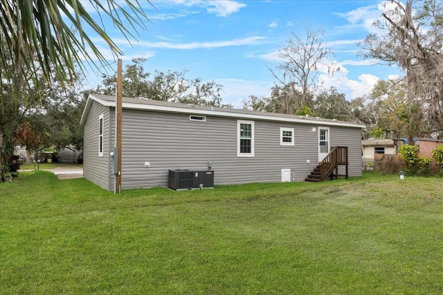 rear view of house featuring entry steps, central AC unit, and a lawn