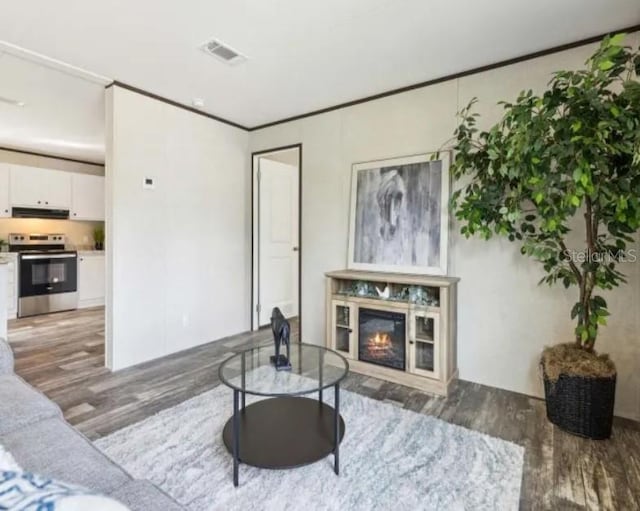 living room with a glass covered fireplace, wood finished floors, visible vents, and ornamental molding