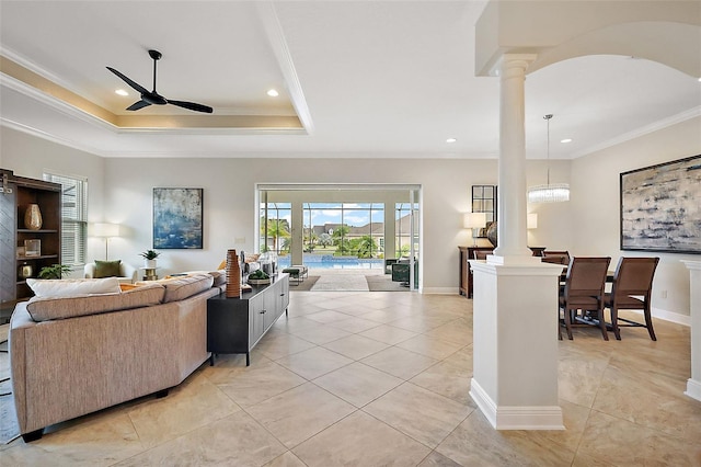 living room featuring baseboards, a raised ceiling, ceiling fan, crown molding, and ornate columns