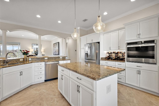 kitchen with appliances with stainless steel finishes, a kitchen island, a sink, and decorative columns