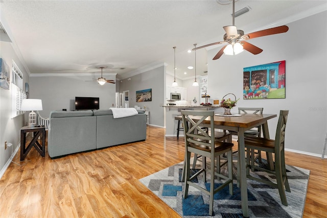 dining room featuring visible vents, baseboards, light wood finished floors, ceiling fan, and ornamental molding