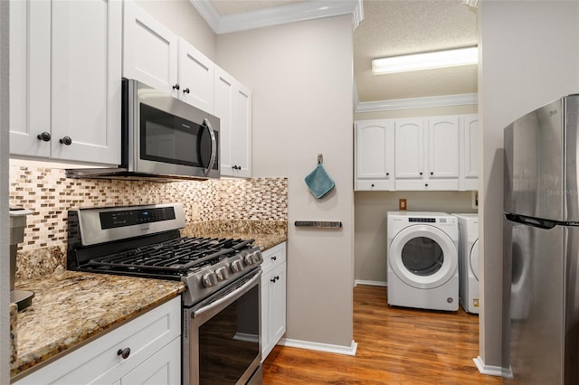 kitchen with light wood finished floors, stainless steel appliances, white cabinetry, crown molding, and independent washer and dryer