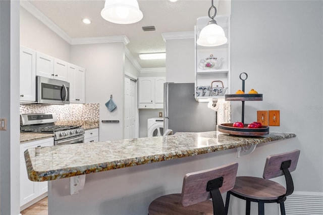 kitchen featuring a breakfast bar, a peninsula, washer / dryer, appliances with stainless steel finishes, and crown molding