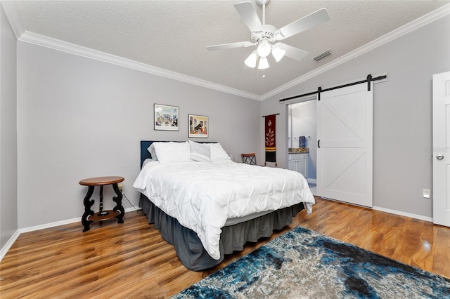 bedroom with visible vents, ornamental molding, a textured ceiling, wood finished floors, and a barn door