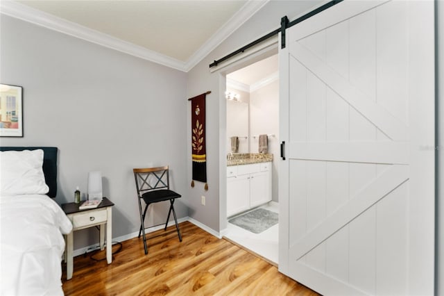 bedroom with ensuite bath, a barn door, crown molding, light wood finished floors, and baseboards