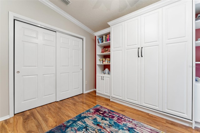 bedroom with a textured ceiling, visible vents, light wood finished floors, and ornamental molding