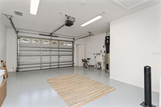 garage featuring visible vents, baseboards, heat pump water heater, a garage door opener, and a sink