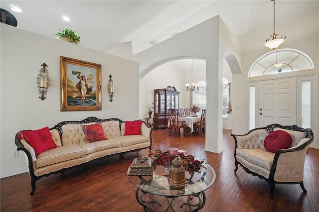 living room with arched walkways, an inviting chandelier, wood finished floors, high vaulted ceiling, and baseboards