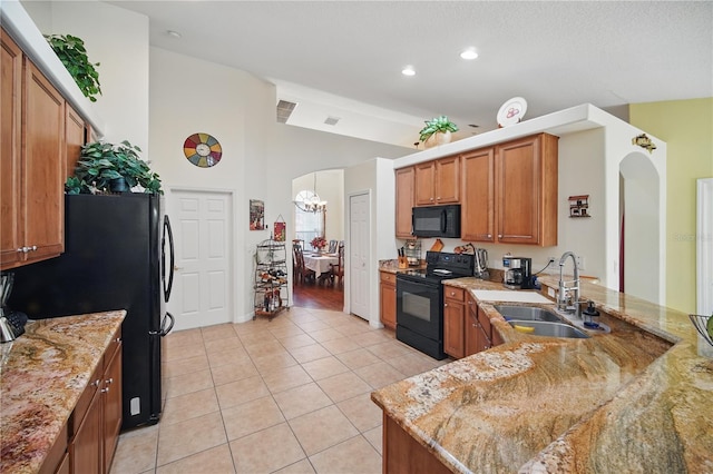 kitchen with light tile patterned floors, arched walkways, brown cabinetry, black appliances, and a sink