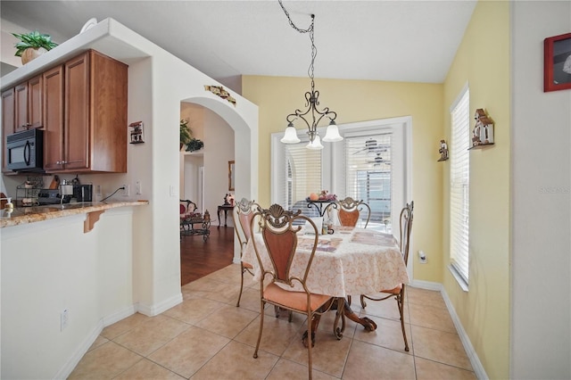 dining area with light tile patterned floors, arched walkways, lofted ceiling, and a notable chandelier