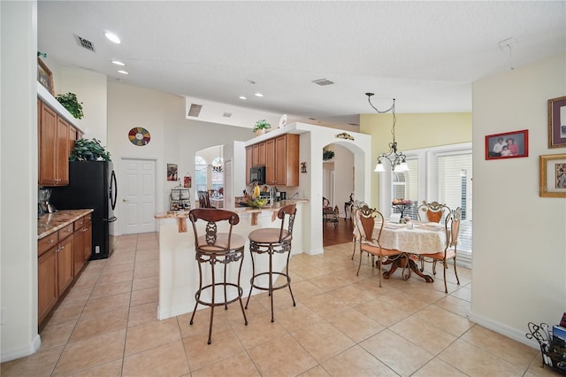 kitchen with arched walkways, vaulted ceiling, brown cabinetry, and visible vents