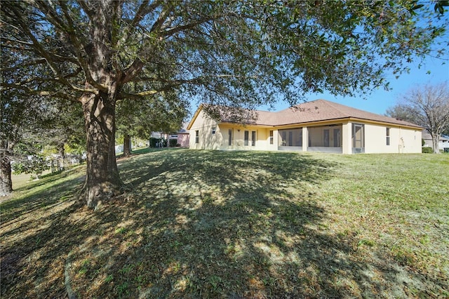 back of house with a sunroom, a lawn, and stucco siding