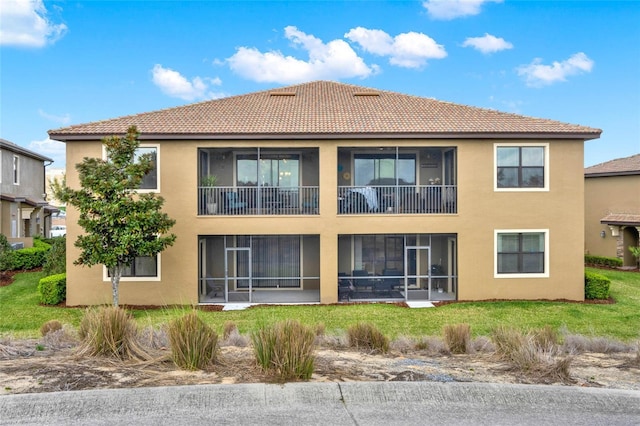 rear view of property featuring stucco siding, a sunroom, and a yard