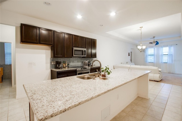 kitchen with dark brown cabinetry, a tray ceiling, light stone counters, stainless steel appliances, and a sink