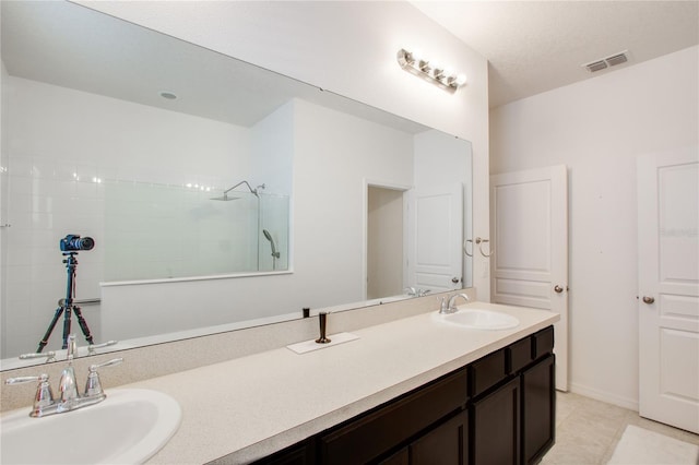 bathroom with a sink, visible vents, tiled shower, and double vanity