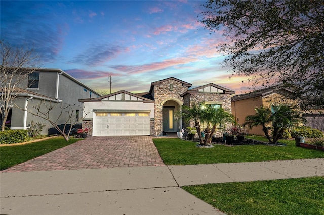 view of front of home with a front yard, an attached garage, stucco siding, stone siding, and decorative driveway