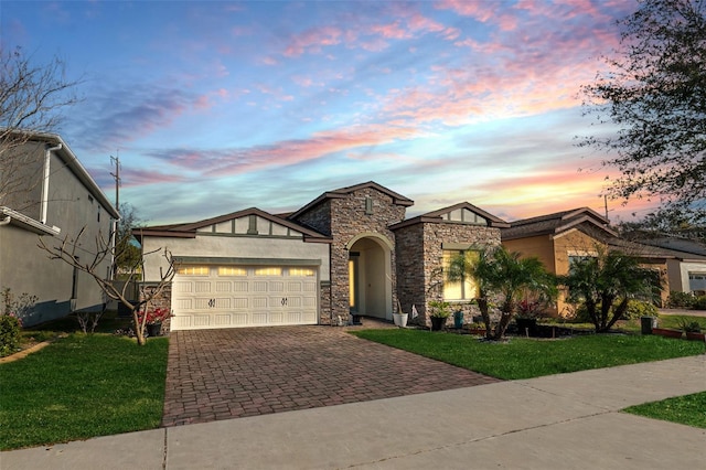 view of front of property featuring a garage, decorative driveway, a front lawn, and stone siding